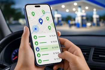 Unas manos sostienen un teléfono celular con una aplicación de mapa y precios de combustible en el interior de un vehículo.