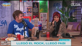 Fabiana Cantilo con cabello rojo y chaqueta de leopardo sentada frente a un micrófono junto a un hombre barbudo en un estudio con paredes de hormigón