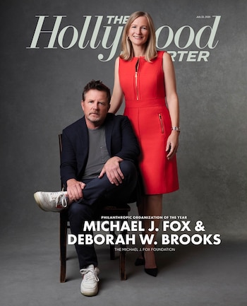 Michael J. Fox sentado en una silla junto a Deborah W. Brooks de pie, ambos frente a un fondo gris. Se ve el logotipo de The Hollywood Reporter
