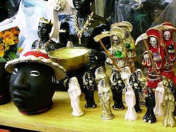 Varias estatuas de la Santa Muerte y figuras con motivos afroamericanos, un cuenco dorado, guadañas y un sombrero con conchas