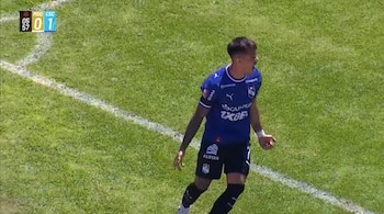 Un futbolista con uniforme azul marino grita en un campo de césped verde cerca de una línea blanca, con un marcador superior que indica cero a uno