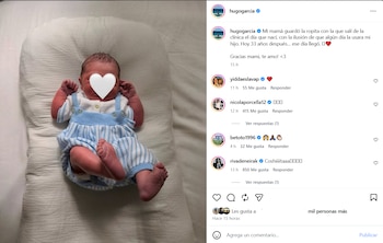 Un bebé recién nacido acostado sobre un cojín blanco. Su rostro está cubierto por un corazón blanco. Viste un enterito de tirantes a rayas celestes y blancas