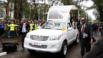 El papa Francisco saluda desde la parte trasera de un vehículo blanco adaptado con placa SCV 1, rodeado por escoltas y público