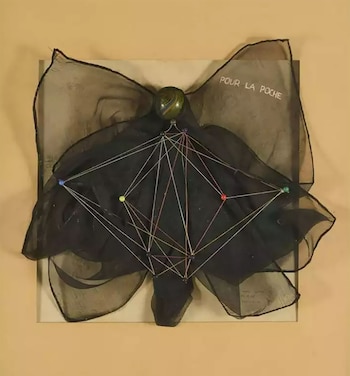 Obra de arte con tela oscura transparente en forma de lazo, una esfera verde y hilos de colores conectados a pines sobre un fondo beige. Título: Pour la poche