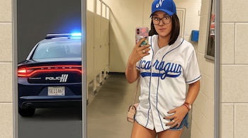 Mujer tomando una selfie en un espejo, viste camiseta de béisbol "Nicaragua" y gorra azul; detrás de ella se refleja un coche de policía de Puerto Rico.