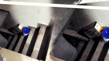 Una escalera de peldaños claros vista desde arriba, con un balde azul y una caja depositados en los peldaños