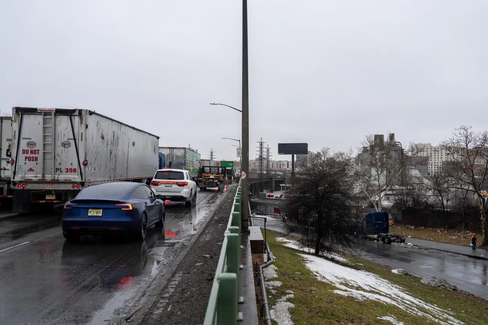 Un día gris y con tráfico denso en la Cross Bronx Expressway, donde coches y camiones transitan por la carretera mojada mientras se observa nieve derretida en los bordes. (David Dee Delgado for The New York Times)