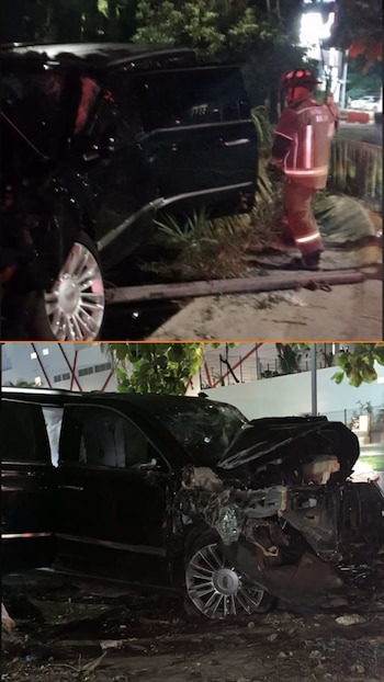 Vehículo negro siniestrado, de noche, con daños severos en la parte delantera y lateral. Un bombero con uniforme de protección está cerca. Vegetación y suelo