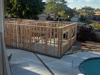 Estructura de madera de una construcción, piscina, patio de concreto, casas residenciales, árboles, montaña y cielo despejado