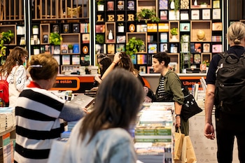 Múltiples personas interactúan con libros en un establecimiento, con estanterías altas llenas de volúmenes y un gran letrero que dice 'LEER'