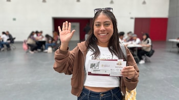 Mujer joven sonriendo con gafas de sol, sosteniendo dos documentos del Gobierno de México y Banco del Bienestar, con la mano derecha levantada.
