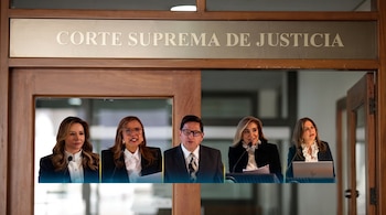 Un letrero de madera con el texto Corte Suprema de Justicia sobre cinco personas con vestimenta formal frente a micrófonos.