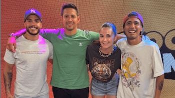 Cuatro personas, tres hombres y una mujer, sonriendo y posando para una foto. Los tres hombres llevan gorras, y la mujer lleva un collar grueso