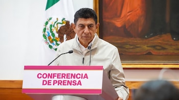 Hombre de mediana edad con chaqueta clara, de pie detrás de un podio con "Conferencia de prensa" y dos micrófonos. Bandera de México y cuadro grande en el fondo.