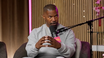 Jamie Foxx viste una sudadera gris y cadenas de plata mientras habla ante un micrófono en un estudio