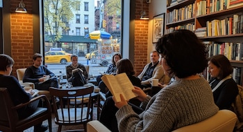 Vista interior de un grupo de personas sentadas leyendo en un club de lectura, con estanterías de libros al fondo y una ventana con vistas a una calle de Nueva York con un taxi amarillo.