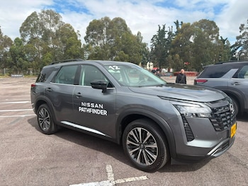 Un vehículo tipo SUV de color gris con la inscripción Nissan Pathfinder en la puerta, estacionado en un espacio asfaltado