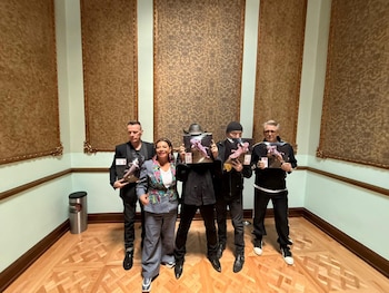 Clara Brugada junto a Larry Mullen Jr., Adam Clayton y dos hombres más, posando en una sala, todos sosteniendo objetos similares a premios