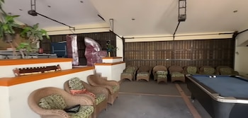 Un salón con una mesa de billar azul, múltiples sillones de mimbre colocados junto a las paredes y plantas de interior
