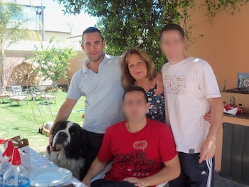 Cuatro personas, incluyendo un hombre con polo azul y una mujer con blusa estampada, junto a un perro San Bernardo en un jardín soleado con césped