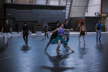 Bailarines con ropa de ensayo realizan posturas y movimientos sobre un escenario amplio de suelo oscuro