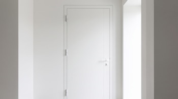 Puerta interior blanca cerrada con manija y bisagras metálicas, instalada entre paredes de tonos claros.