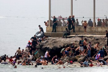 Tras alcanzar la costa, decenas de personas escalan las rocas del espigón para acceder a la ciudad. Las imágenes recuerdan a las escenas vividas durante la crisis migratoria de mayo de 2021. (EFE)