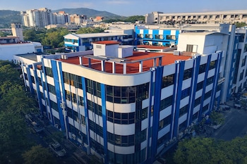 Edificio de varias plantas con franjas azules y blancas, ventanas de cristal, techos rojos, edificios en el fondo, árboles, calle y automóviles.