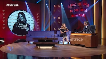 Marcela Kloosterboer sentada en un sofá morado en un set de televisión, frente a un presentador en un escritorio. Una pantalla circular muestra su imagen