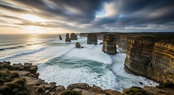 Perspectiva panorámica de formaciones rocosas erosionadas en el océano, con acantilados a la derecha, mar agitado y cielo con nubes dinámicas, bajo luz dorada.