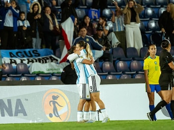 Cuatro jugadoras de fútbol femenino en el campo. Dos de Brasil con camisetas amarillas y shorts azules, dos de Argentina con camisetas celestes y blancas a rayas