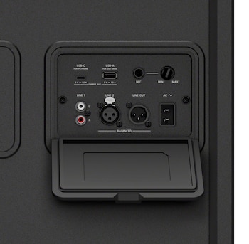 Panel posterior de un altavoz negro con puertos USB, RCA, conector de entrada y salida XLR, una perilla de volumen y una tapa plástica abierta