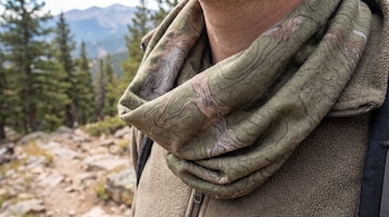 Primer plano del cuello de una persona que lleva una braga tubular verde con mapa topográfico en un paisaje de montaña.