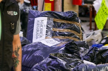Bolsas negras con etiquetas "MERCANCÍA ASEGURADA" y el logo del IMPI se ven junto al brazo de una persona con tatuaje en un operativo