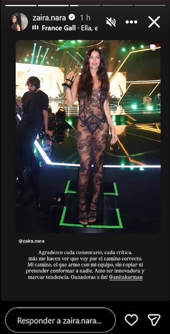 Zaira Nara sonríe en un escenario, sosteniendo un trofeo. Viste un enterizo de encaje negro transparente con diseños florales, con tacones negros