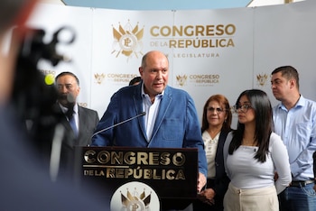 Un hombre con chaqueta azul habla frente a un micrófono en un podio con las letras Congreso de la República, rodeado de otras personas
