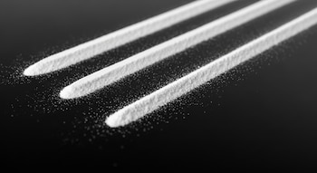 Plano detalle de una mesa negra con tres líneas blancas de polvo dispuestas de forma ordenada.