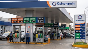 Surtidores de combustible con letreros de precios, mangueras de colores, vehículos estacionados y la señalización de Osinergmin bajo un techo.