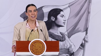 Una mujer habla desde un podio de madera con dos micrófonos y el escudo de México, frente a una ilustración de una mujer con una bandera.