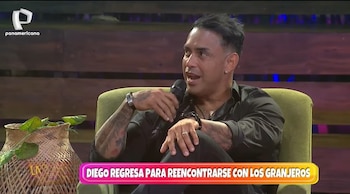 Diego Chávarri sentado en un sillón verde, sosteniendo un micrófono, con tatuajes visibles en sus brazos y una pulsera plateada. Lleva camisa negra