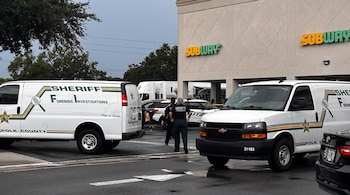 Dos camionetas del Sheriff de Polk County, personal forense, un edificio con letrero de Subway y un coche negro en un estacionamiento