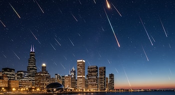 Paisaje nocturno de Chicago con la silueta de rascacielos iluminados y el lago, bajo un cielo estrellado atravesado por múltiples lluvias de meteoros de colores.