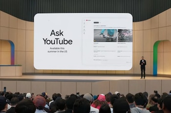 Sundar Pichai de pie en un escenario frente a una pantalla grande que muestra "Ask YouTube" y resultados de búsqueda, con una audiencia visible en primer plano