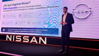 Un hombre en traje habla en un escenario frente a una pantalla azul con el logotipo de Nissan y texto en español