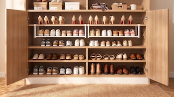 Armario de madera abierto con varios estantes que contienen zapatos de tacón, zapatillas deportivas, mocasines, botas y cajas de almacenamiento.
