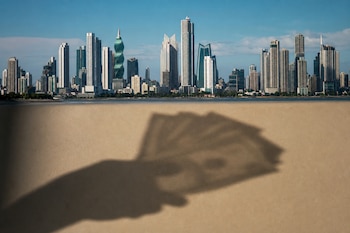 Sombra de una mano con dinero proyectada sobre una superficie beige con los rascacielos de Ciudad de Panamá al fondo.