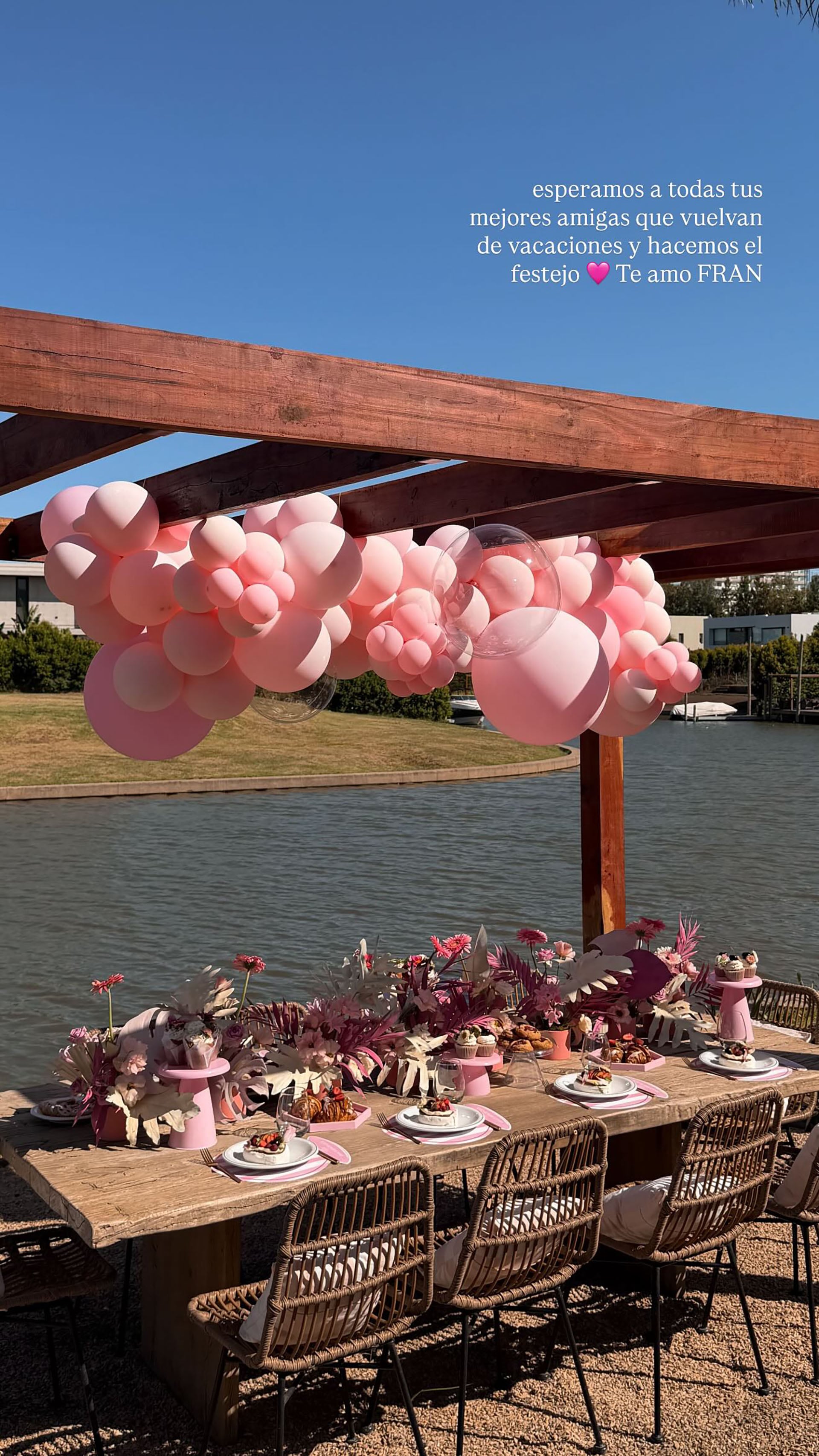 Una mesa de madera decorada con globos rosados y arreglos florales, junto al lago, recibe a los invitados (Instagram)