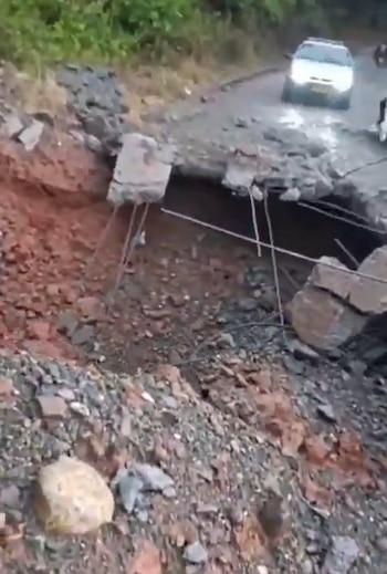 Un gran hueco en una carretera asfaltada muestra varillas de hierro expuestas, escombros de concreto, tierra y un automóvil al fondo
