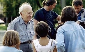 Eugene Lazowski, un anciano con gafas y camisa de vestir clara, hablando con varias personas, incluyendo niños y adultos, al aire libre