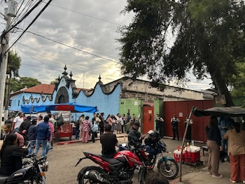 Una multitud reunida de noche en una calle frente a agentes de policía con escudos, con postes de luz y vehículos al fondo